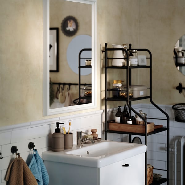 A PINGSTSYREN mirror with a white-painted, solid pine frame hangs above a white wash-stand in a traditional-styled bathroom.