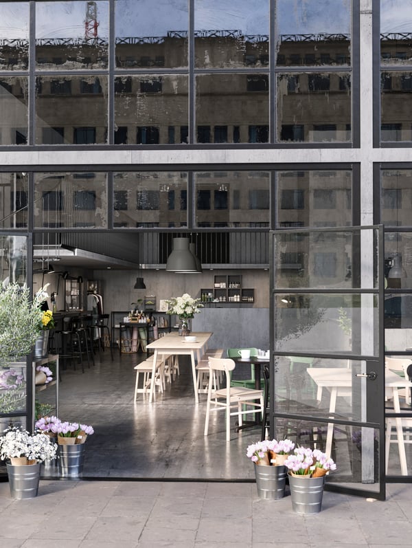An open plan cafe, shop and co-working space framed by open glass doors. Flowers are on the table and by the doors.