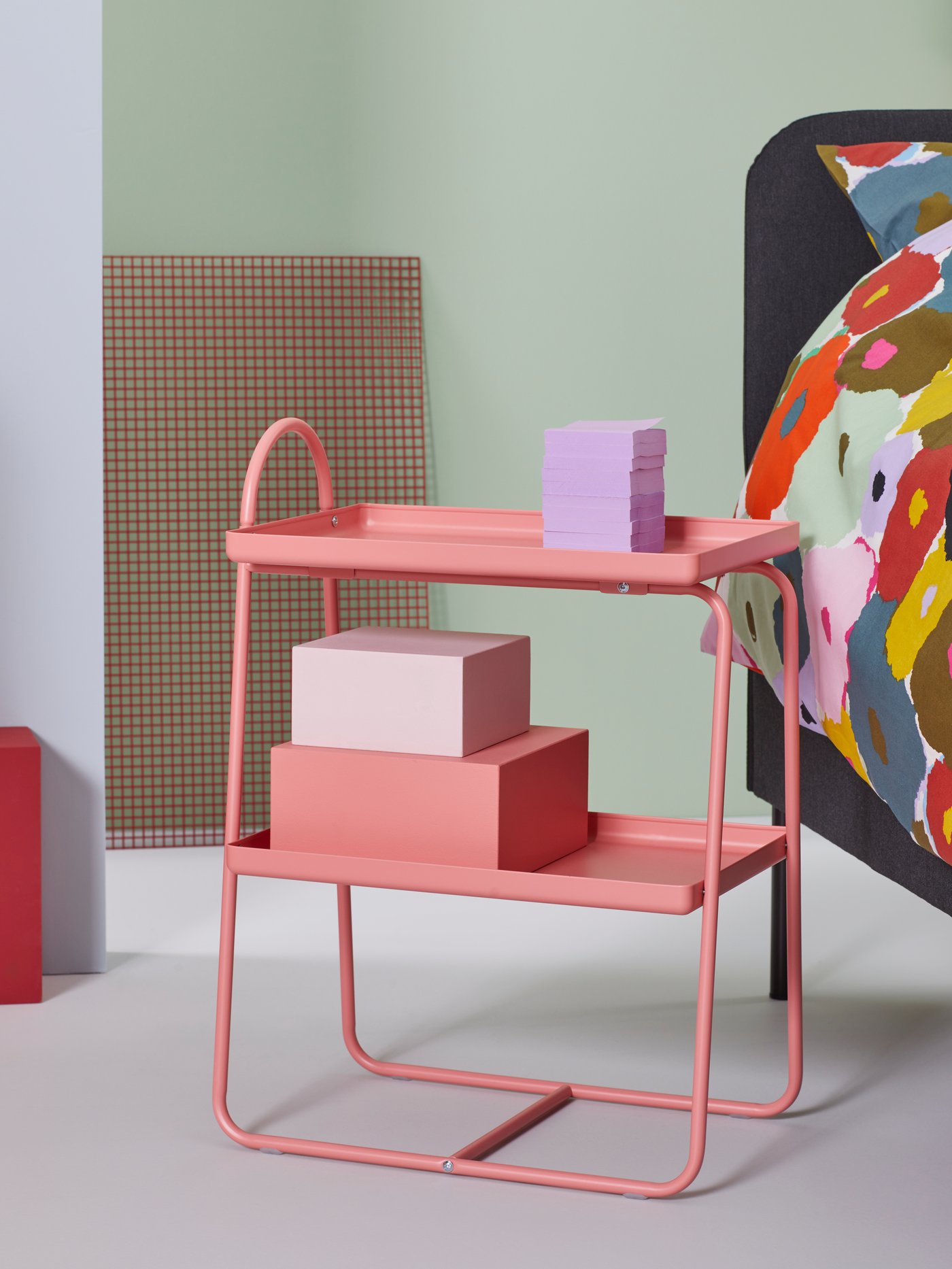 In a green room Room there is a pink shelf in the middle and in the back you can see a black sofa.