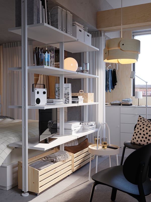 A white ELVARLI storage combination at the end of a white NORDLI bed, with a birch SÖDÅKRA pendant lamp hanging beside it.