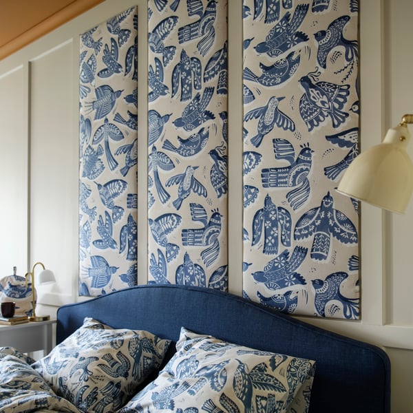 Ett ljusgrått/blått BITTERSÖTA påslakanset med örngott på en säng, under väggpaneler gjorda av BITTERSÖTA färdigskuren textil.