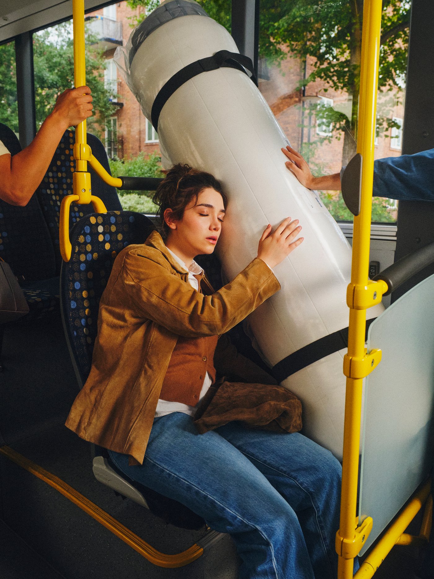 VALEVÅG-pussijousipatja on alkuperäisessä rullapakkauksessaan bussin ikkunapaikalla. Patjaa vasten nojannut henkilö torkkuu rauhallisesti matkan aikana.