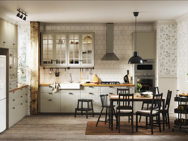Ett stort öppet kök beige luckor. Framför står ett bord med svarta stolar.