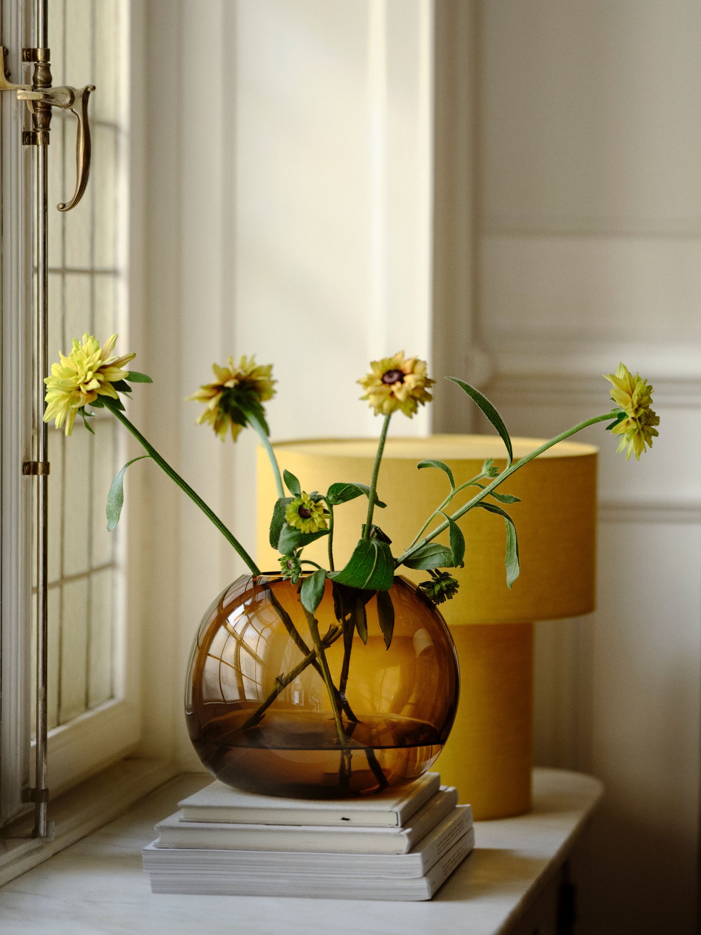 Eine gelbe/textile STOCKHOLM 2025 Tischlampe und eine braune Vase aus Glas