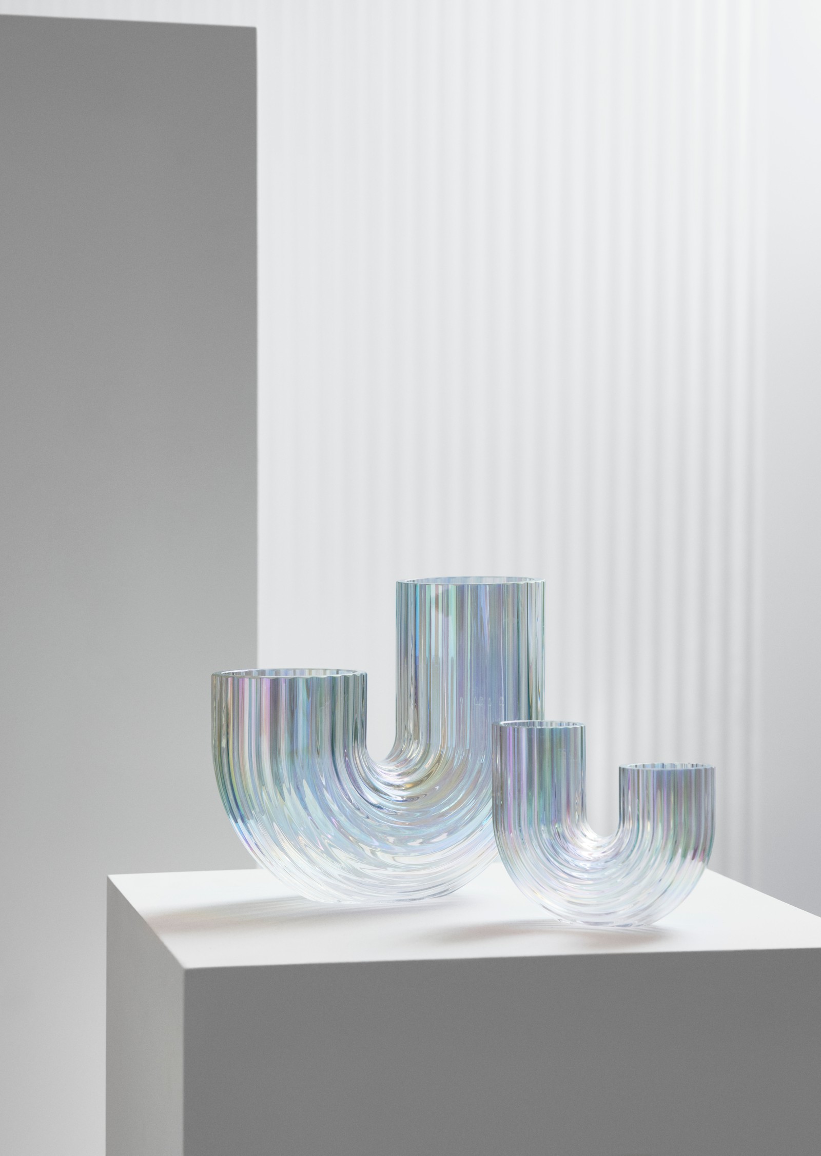Two different-size, mother-of-pearl-coloured RÄFFELBJÖRK glass vases sit on a white box in a brightly lit room.