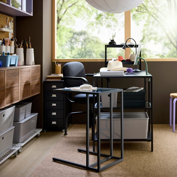 Home workspace setup with black-brown VITTSJÖ desk, a chair and storage drawers, placed by a bright window.