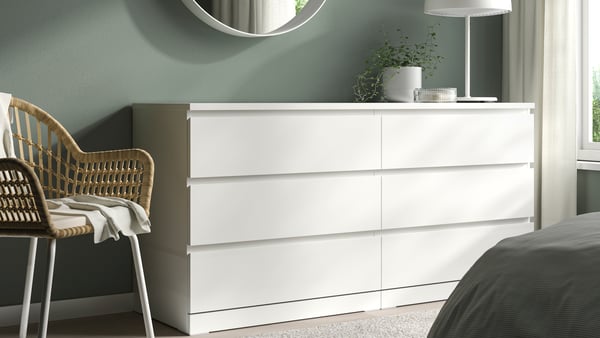 A white MALM 6-drawer dresser in a bedroom, with a rattan chair beside it