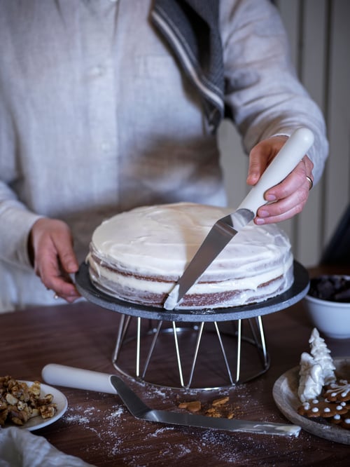 Eine Person verziert einen Kuchen auf einem BAKGLAD Kuchenteller mithilfe eines LÄTTBAKAD Palettenmessers.