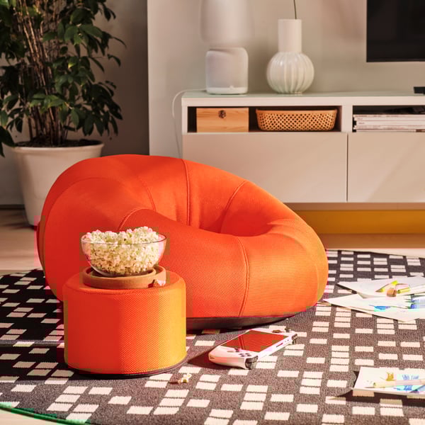 Una sala con un sillón naranjo y al costado una mesa lateral con palomitas de maíz. 