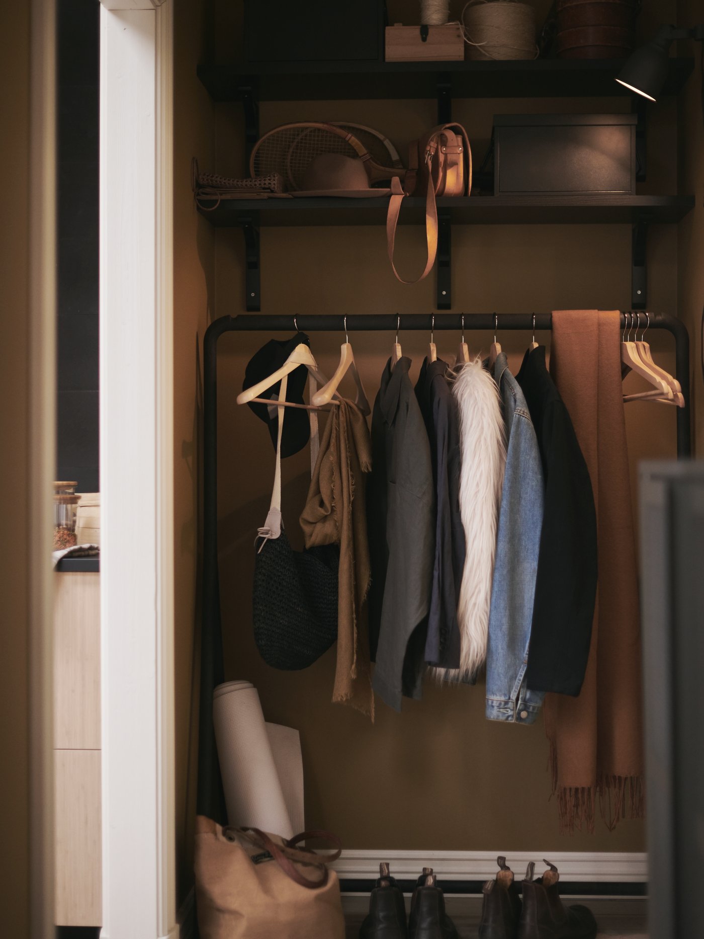 A black TURBO clothes rack, in combination with wall-mounted shelves, creates a clothes storage solution in a hallway.