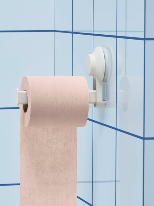 Nahaufnahme eines weißen TISKEN Toilettenpapierhalters mit Saugnapf an einer blau gefliesten Wand mit einer Rolle Toilettenpapier.
