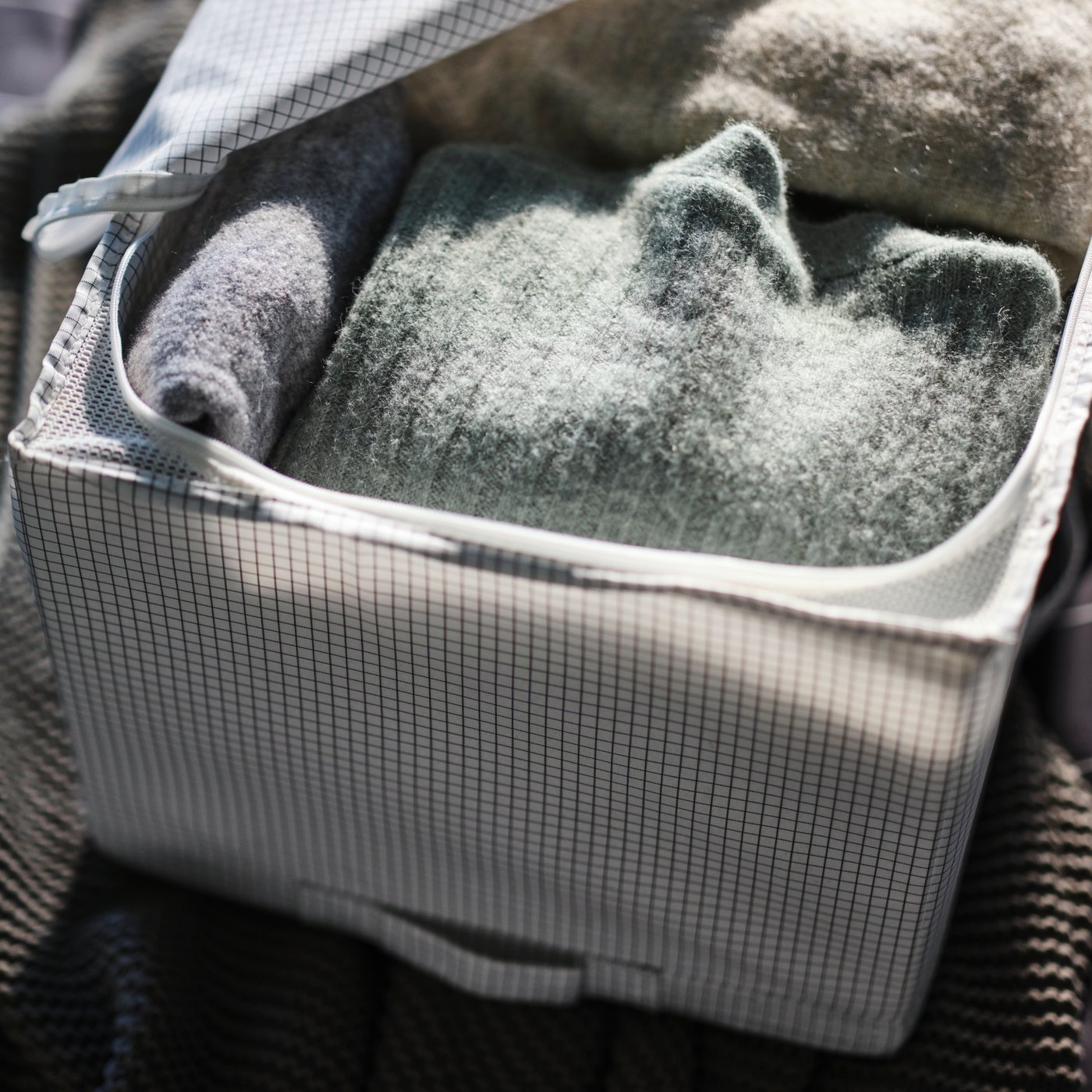 A white-grey STUK storage case, partially open, revealing rolled up winter clothes inside.