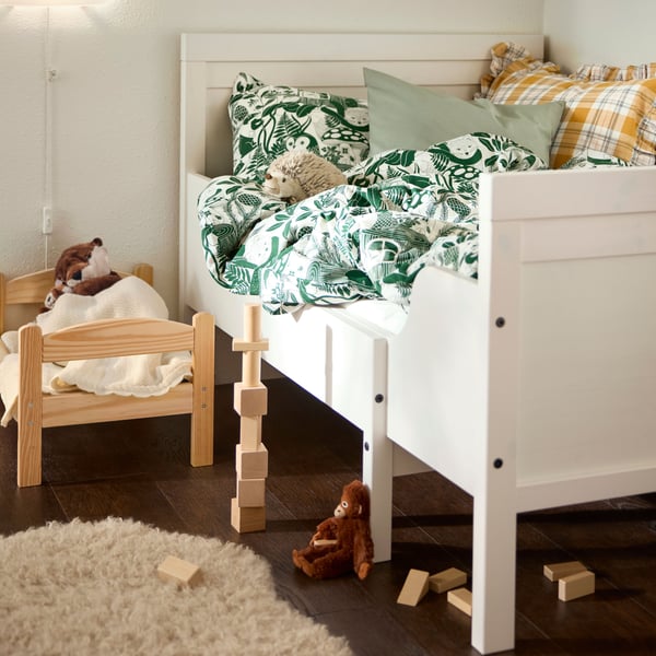 A children’s room in daylight with toys on the floor by a white SUNDVIK extendable bed with green and white bed linen on it.