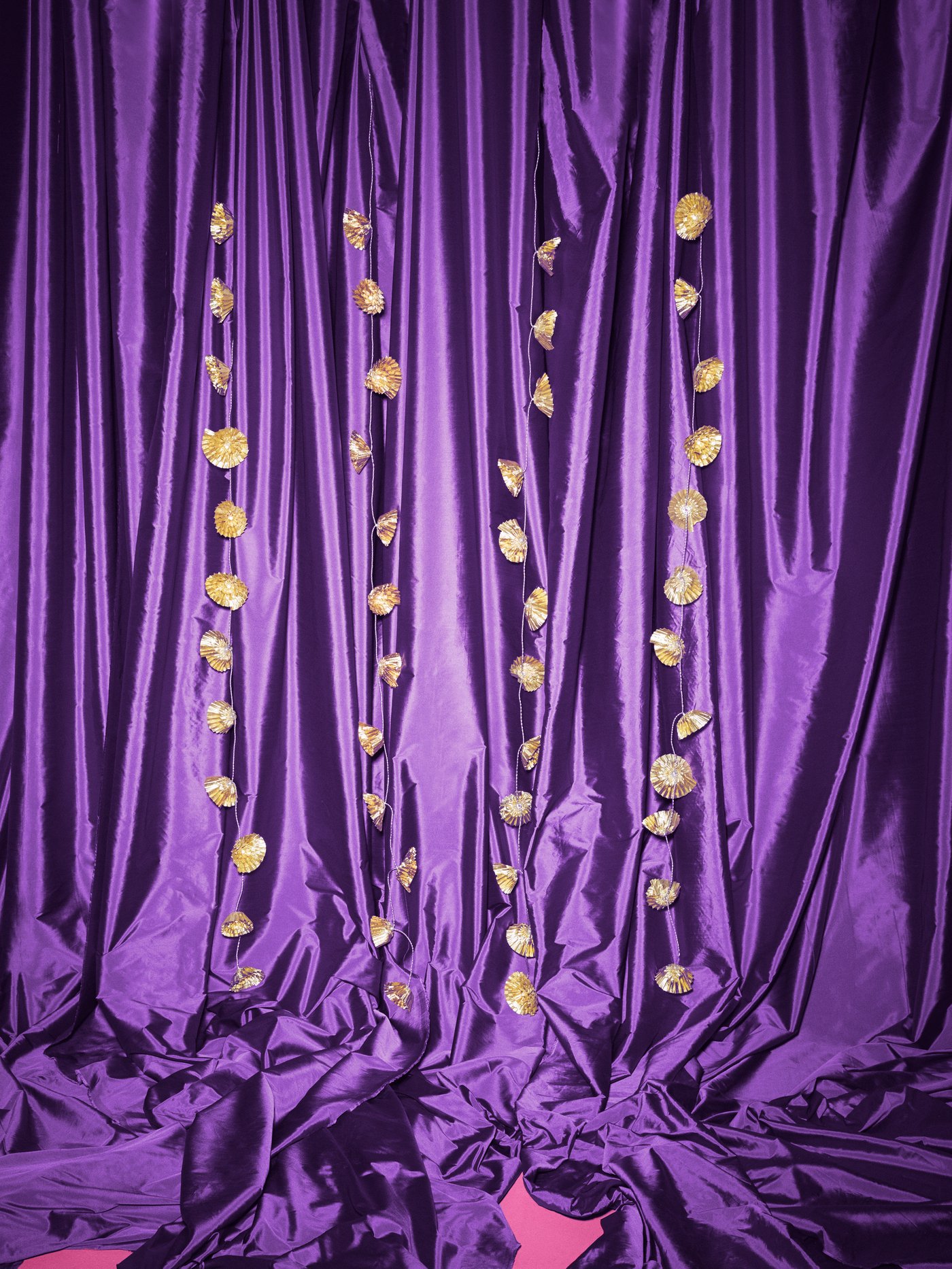 Gold KARISMATISK lighting chains in flower shapes hang downwards against a purple satin backdrop.