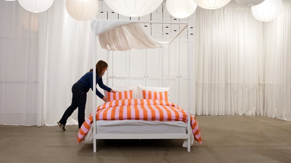 En IKEA medarbetare bäddar en säng med randiga påslakan.