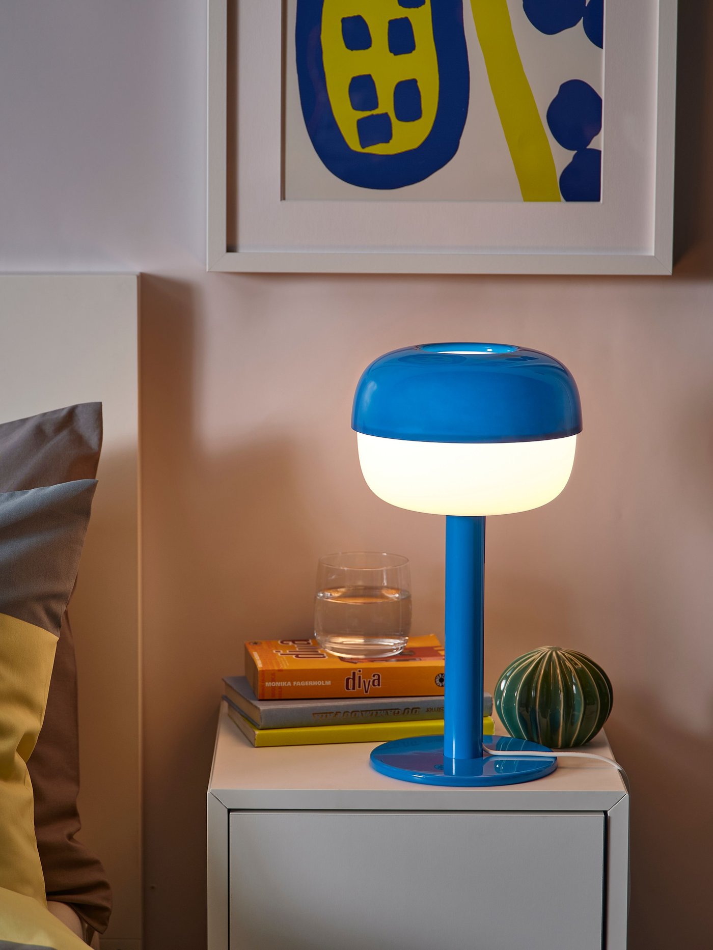 Llum de taula BLÅSVERK de color blau sobre una tauleta de nit EKET.