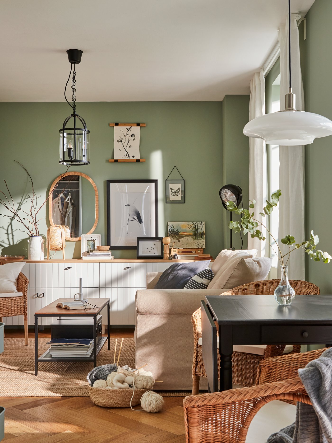Ein kleines Wohnzimmer mit grünen Wänden, einem Sofa, einer kleinen Essecke, gerahmten Postern und Bildern an der Wand.