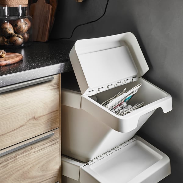 A white SORTERA waste sorting bin with open lid to show newspapers inside, beneath a shelf of glass jars of red preserves.