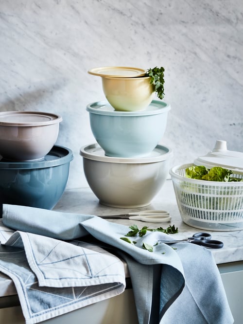 A kitchen worktop with stacks of GARNITYREN lidded bowls, along with a TOKIG salad spinner, scissors and SANDVIVA tea towels.