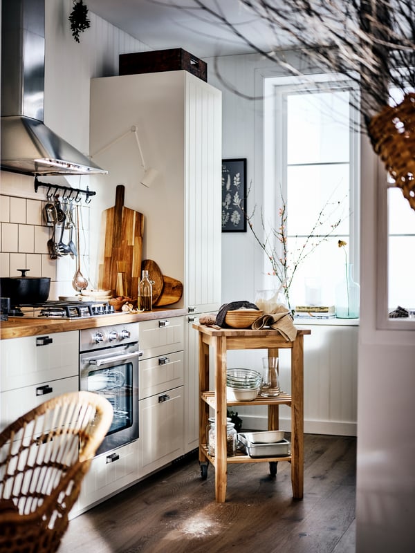 A country-style kitchen with a wood counter top and beige cabinets, and a birch trolley in the middle of the room.