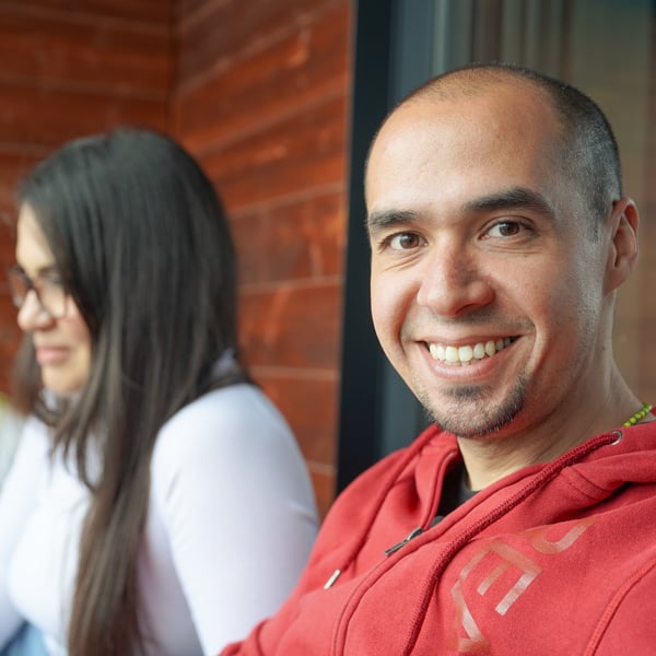 Edgar sits outdoors in his red shirt and smiles at the camera.