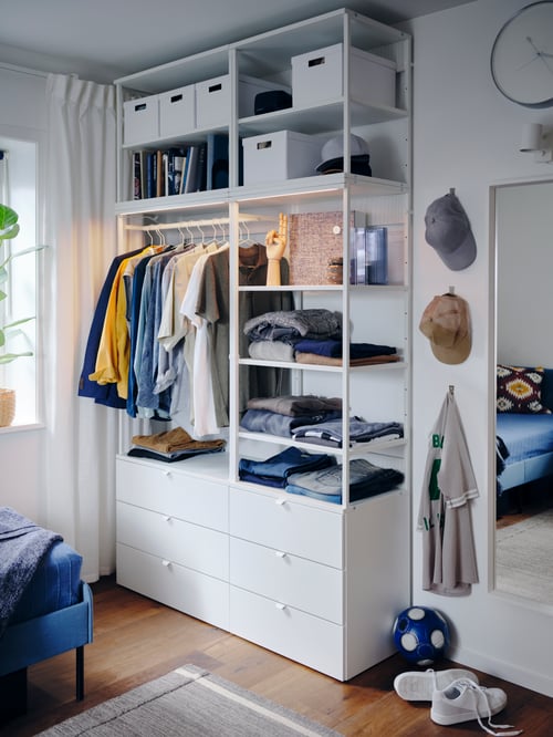 Bedroom with a white wooden wardrobe with six drawers storing multiple storage boxes with lid, next to a rectangular mirror.
