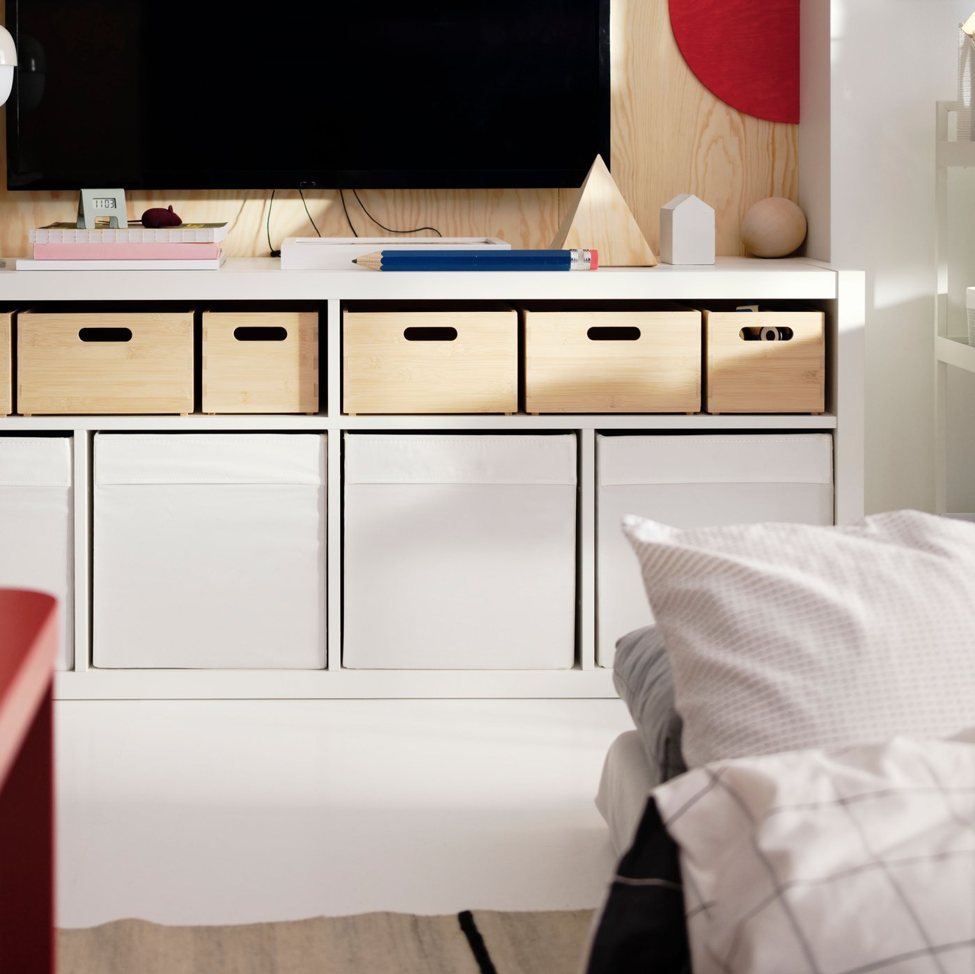 A wall-mounted TV above a white KALLAX TV bench with UPPDATERA storage boxes in light bamboo in the top shelves.