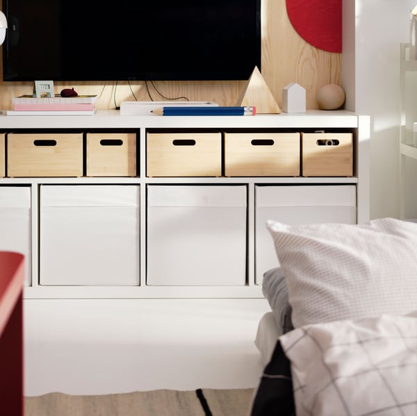 A wall-mounted TV above a white KALLAX TV bench with UPPDATERA storage boxes in light bamboo in the top shelves.