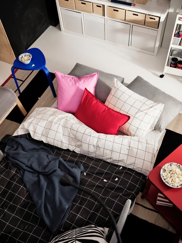 A blue KYRRE still on the side of a bed with black and white bedding and colourful cushions.