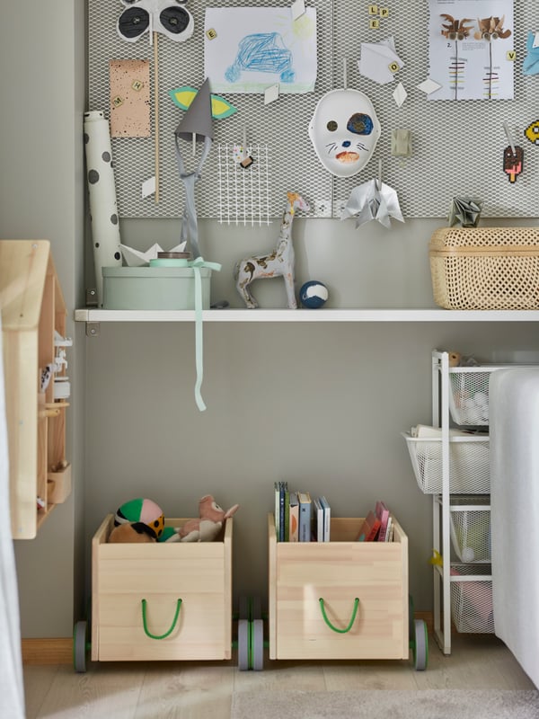 Two FLISAT toy storage units in solid pine with gray wheels and green handles store children’s books and more.