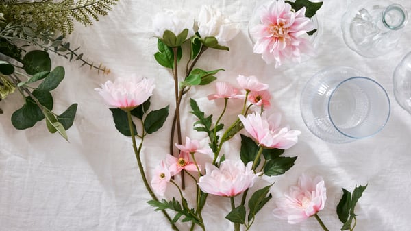 Des fleurs artificielles SMYCKA (pivoine blanche, dahlia rose et coquelicot rose) sur une surface blanche.