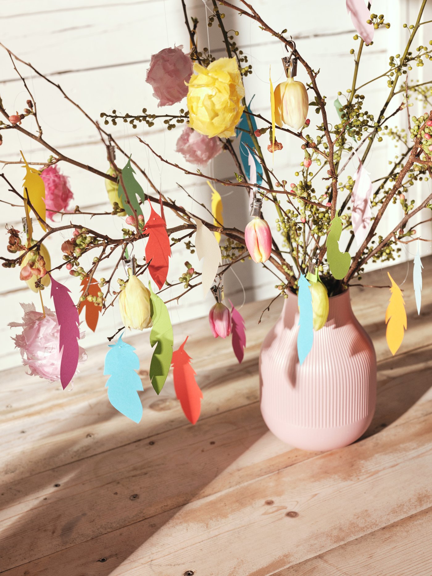 En pink GRADVIS vase fyldt med grønne grene dekoreret med påskepynt.