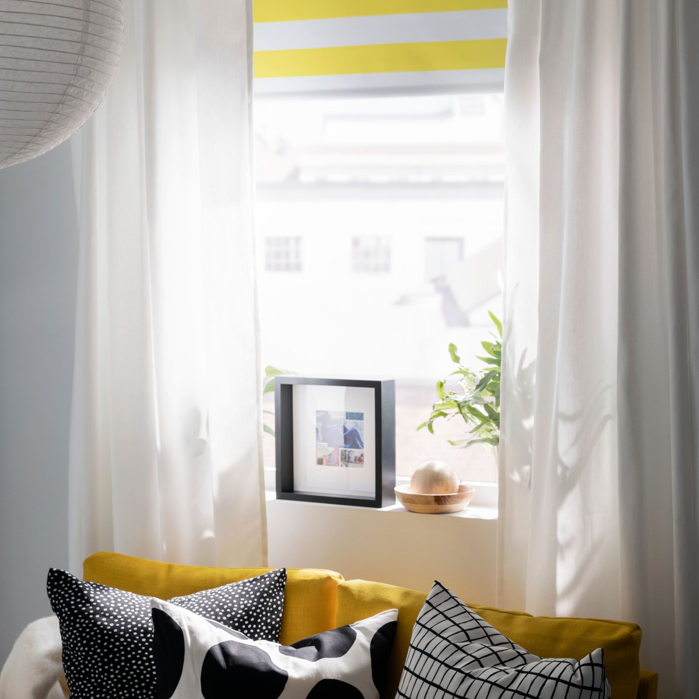 A striped FRIDANS block-out roller blind and GINSTMOTT curtains hang in a window above a yellow FRIDHULT sofa-bed.