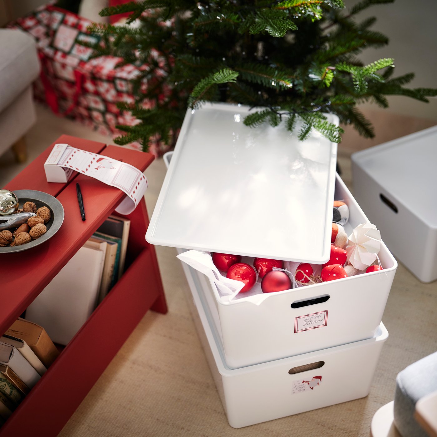 A white KUGGIS storage box with a lid slighty open to show Christmas tree decorations.