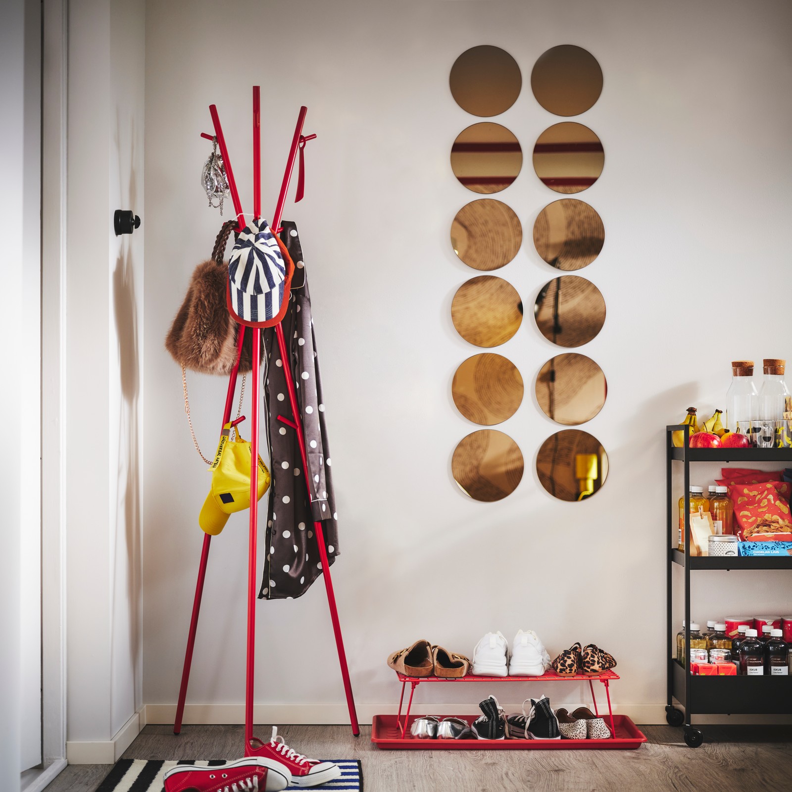 Crveni EKRAR stalak za šešir i kaput, GREJIG stalak za obuću i BAGGMUCK podmetač za cipele nalaze se pored vrata, a na njima su odeća za napolje, torbe i obuća.