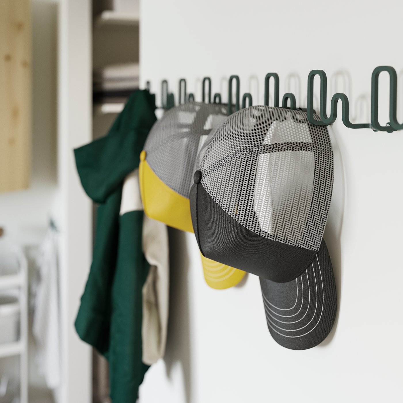 JORDMÅNEN krog på en hvid væg i mørkegrå-grøn, med to kasketter og en jakke hængende på knagerne.