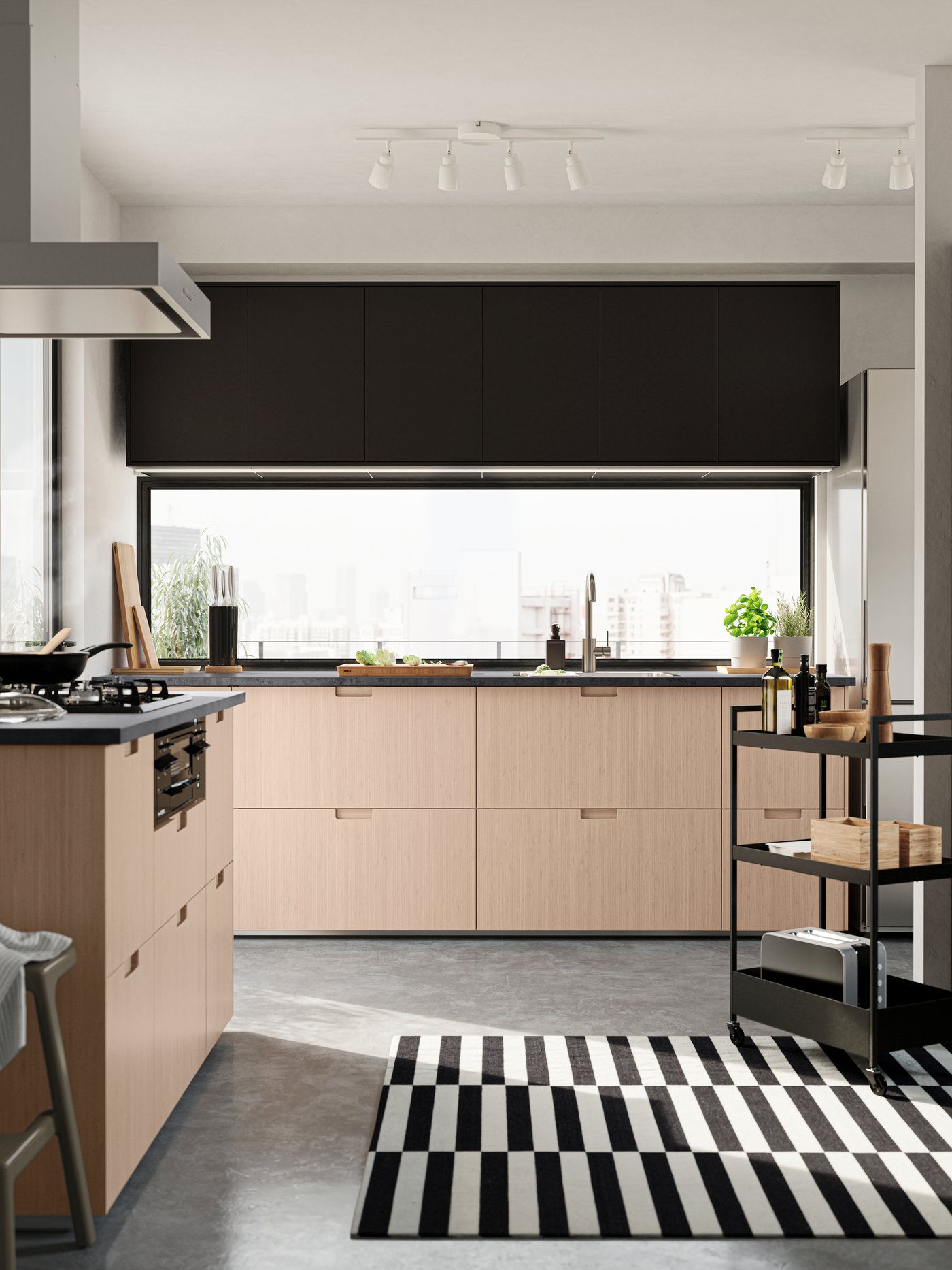 An open-plan kitchen with FRÖJERED fronts in light bamboo. There is a NISSAFORS trolley with condiments, boxes and a toaster.