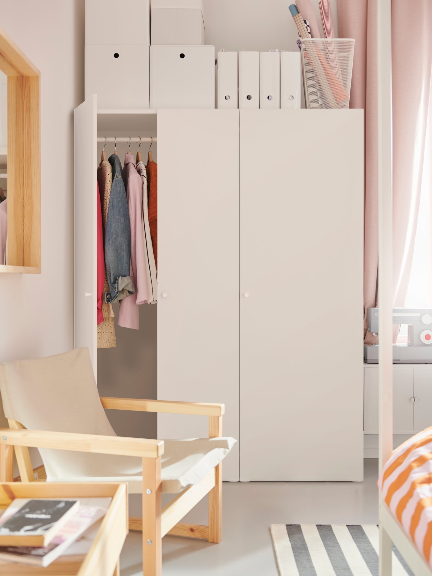 Белый трёхдверный шкаф PLATSA в светлой спальне с одеждой на вешалке и коробками сверху. Одна дверца открыта.