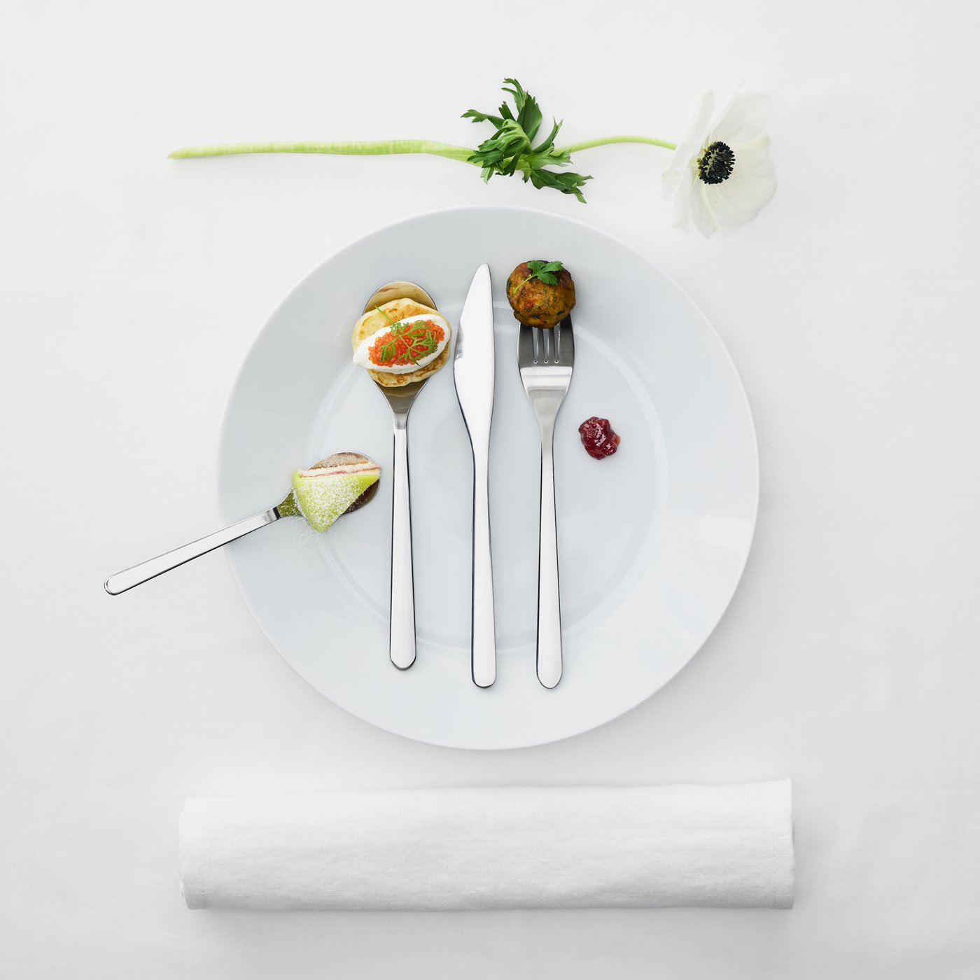 Et sæt FÖRNUFT bestik oven på en hvid tallerken. På bestikket er der forskelligt mad, som kage og kaviar.