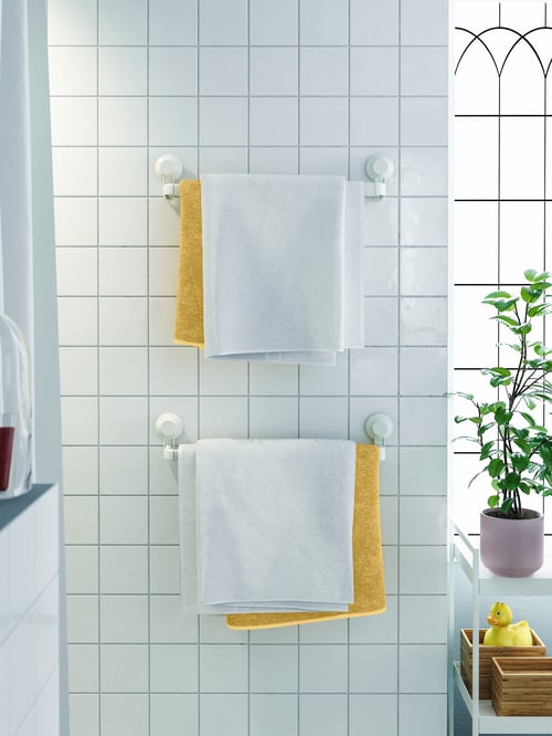 Baie cu 2 suporturi albe pentru prosoape cu ventuză din aluminiu, care susțin mai multe prosoape de baie, lângă un cărucior.