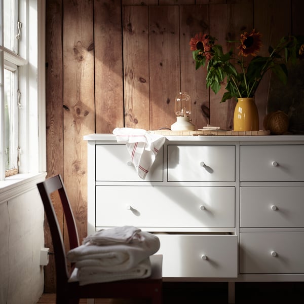 A white GULLABERG chest of 8 drawers against wooden wall panels with plants and small items arranged on top in a bedroom.