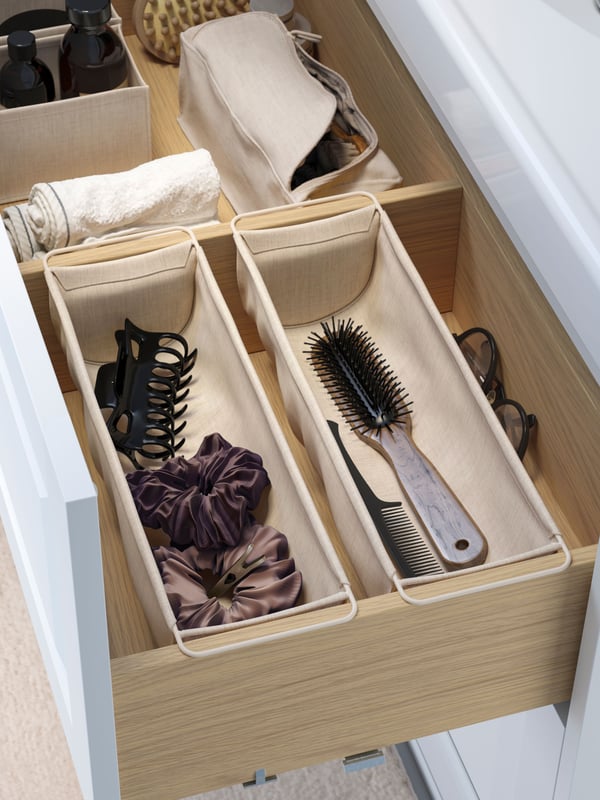 The top drawer of a bathroom wash-basin is open and there are two beige BOLLÖSUND drawer organisers hanging on the inside.