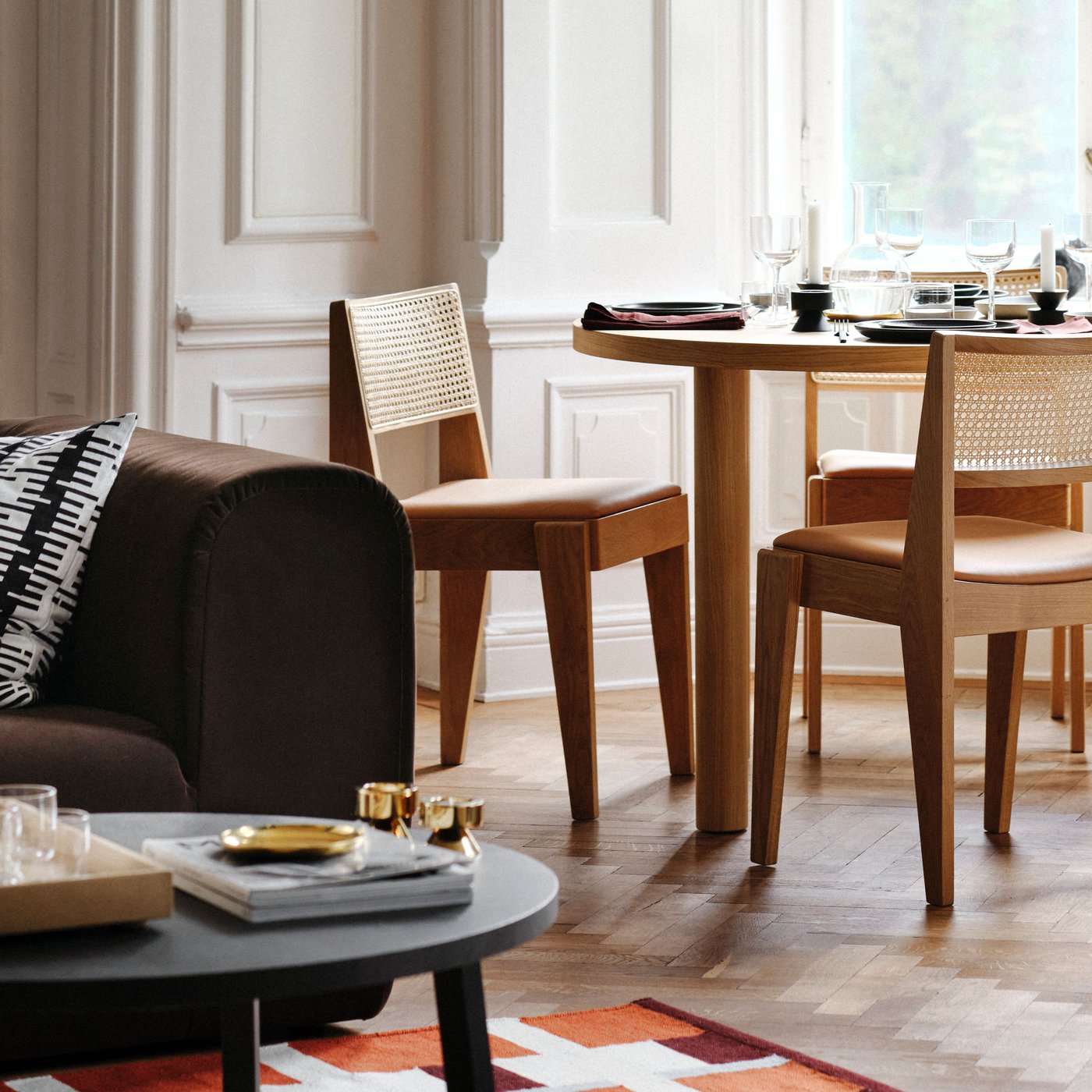 A living room dining set with an oak veneer STOCKHOLM 2025 table and oak and rattan chairs placed by large bay windows.