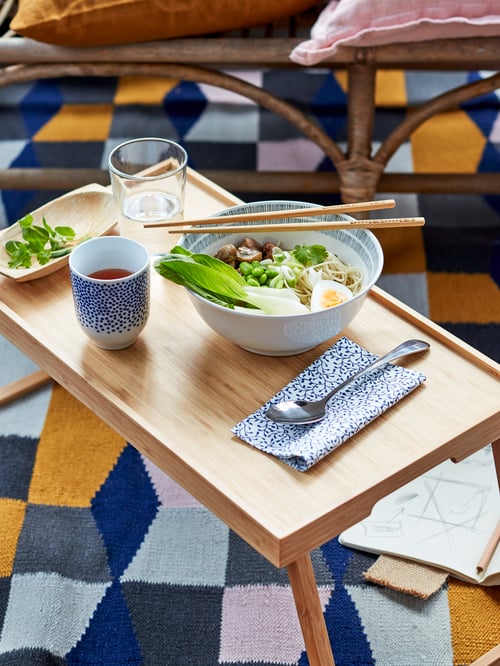 Close-up of a RESGODS bed tray with an ENTUSIASM mug with coffee, ÅTERBLICK bowl with salad, TREBENT chopsticks, and glass.