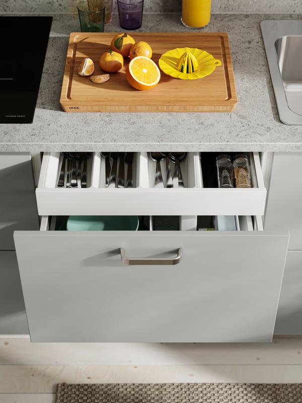 The HAVSTORP light grey kitchen cupboard door with a silver handle, with a drawer opened to display cutlery and kitchen tools.
