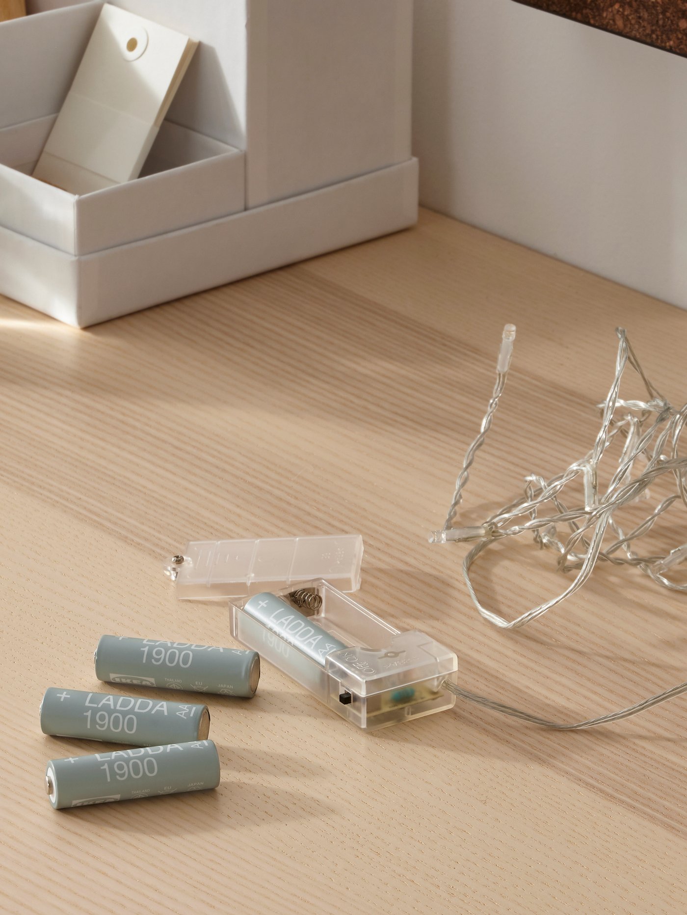 Three AA LADDA rechargeable batteries lie on a surface near the battery box of a lighting chain which contains one battery.