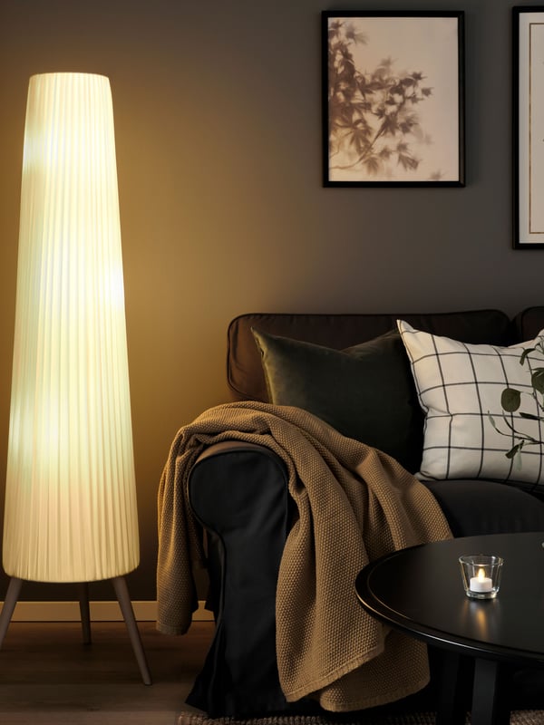 A beech/white ÖKENSAND floor lamp next to a  dark-grey sofa