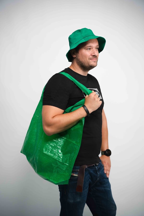 Person i svart t-shirt och blå jeans med grön hatt och stor grön axelväska – urban stil med fokus på personlig accessoar och hållbar livsstil.