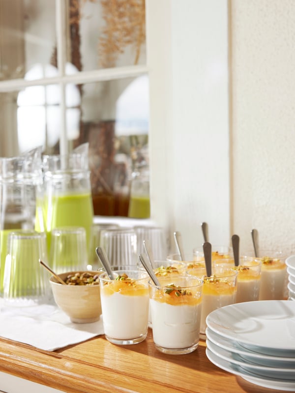 Mesa con postres y platos, jarra de jugo y un mantel de color blanco.