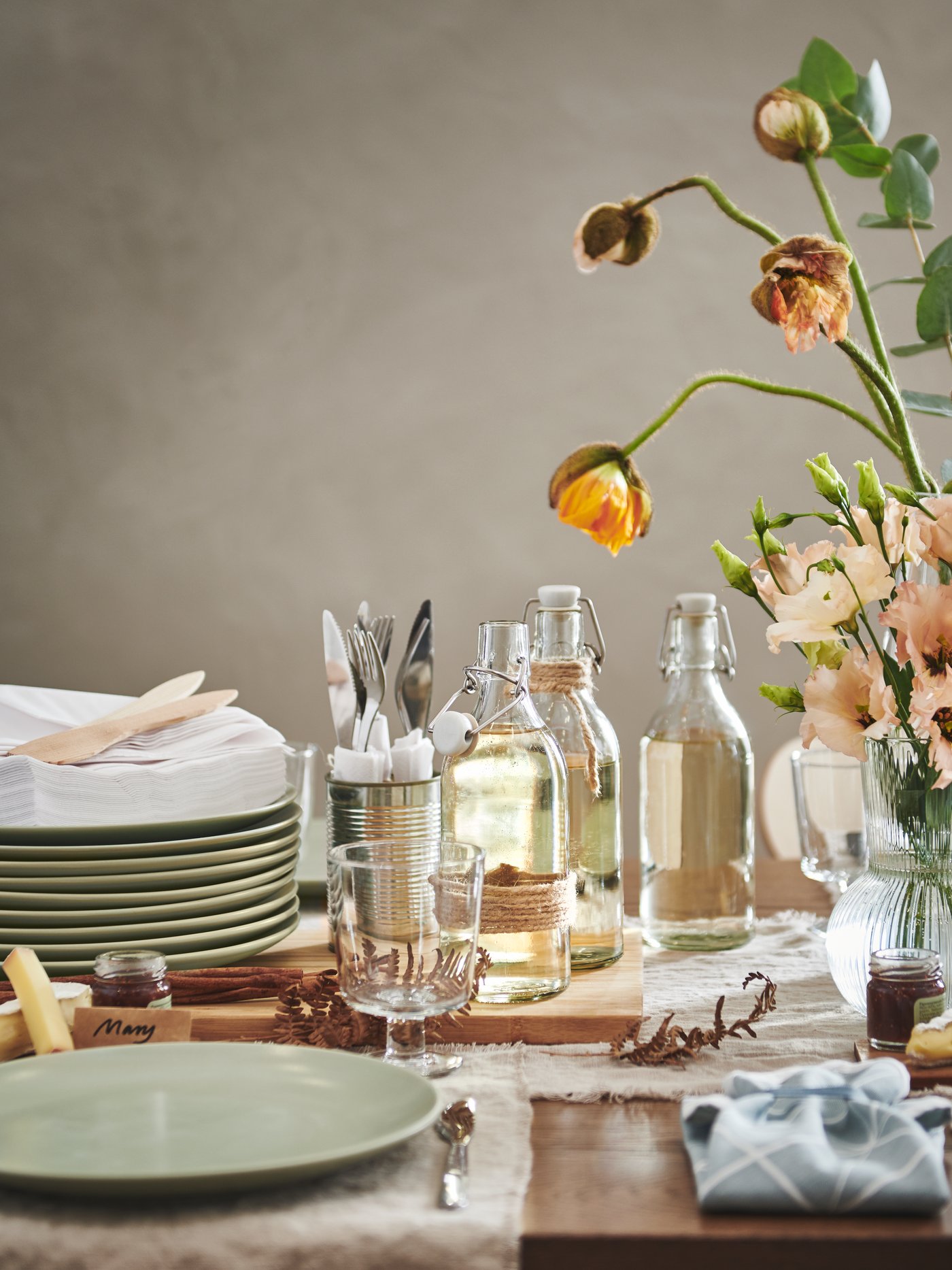 table avec des assiettes vertes empilées , des carafes d'eau et un bouquet de fleur posé sur le côté